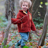 Child stood in a forest wearing an organic red ginger zipped fleece jacket with a big yellow pocket from Little Green Radicals, made from recycled polar fleece, available now at Babipur.