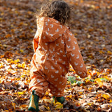Back of baby playing in a forest wearing a Hooded Waterproof Winter Suit in Gold Ducks print, by Little Green Radicals, made from recycled bottles with and a cosy polyester fleece, with a pair of Fairtrade rubber wellies, available to buy at Babipur.