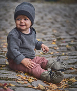 A child sitting on a cobbled surface and wearing the Mamalila quilted Berlin booties in Khaki available at Babipur.