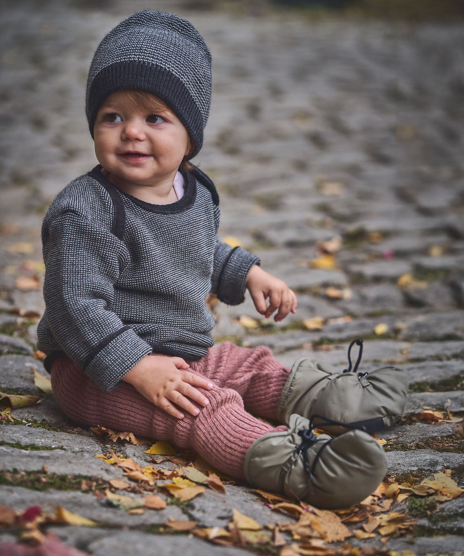 A child sitting on a cobbled surface and wearing the Mamalila quilted Berlin booties in Khaki available at Babipur.