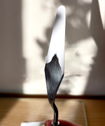 A adult hand holding the Natural Earth Paint palette knife with wooden handle showing white paint underneath