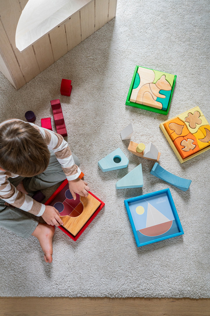 Child playing with Grimm's colorful wooden shape blocks and puzzles on a carpeted floor.