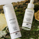 The scent free, soothing and organic Nordic Roots Truffle Night Cream and Hyaluronic Booster Serum laid out on a mossy background with chanterelle mushrooms