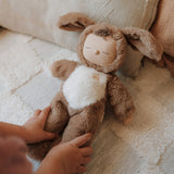 A child tucking a Olli Ella cozy dinkum dog Digby doll in bed. This cosy and fluffy toy doll has a sleeping face, cute floppy ears and available at Babipur