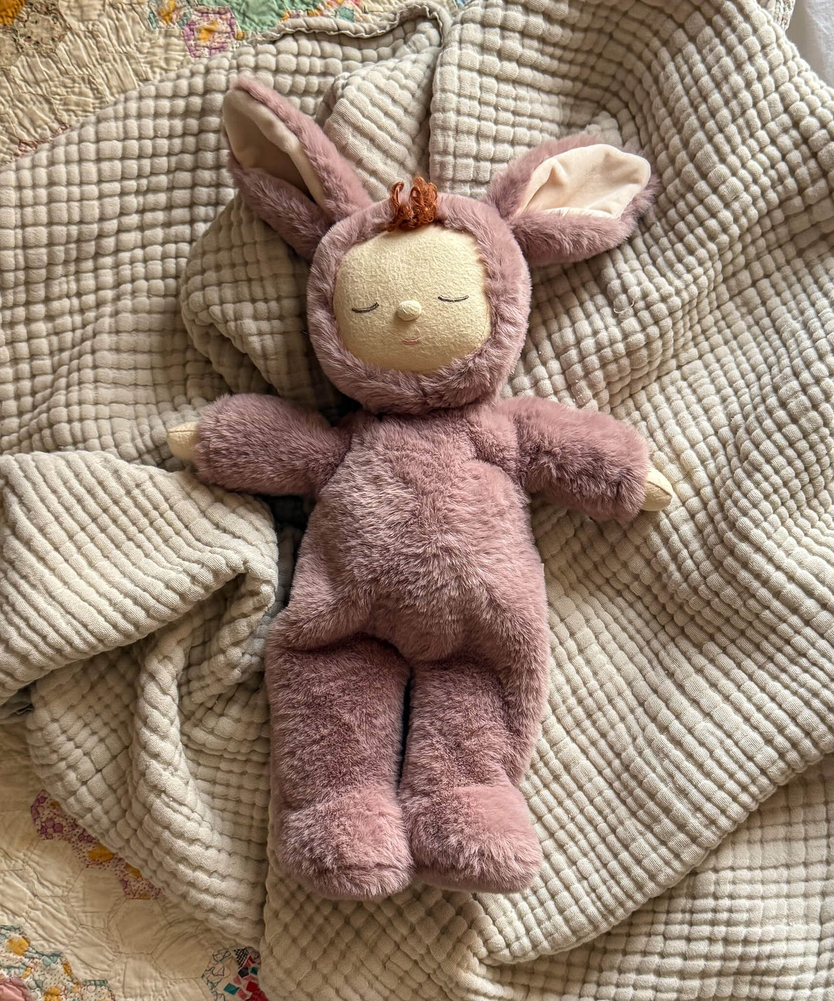 Olli Ella cozy dinkum bunny pickle doll in mauve colour lying on top of a soft blanket. This fluffy toy is available at Babipur