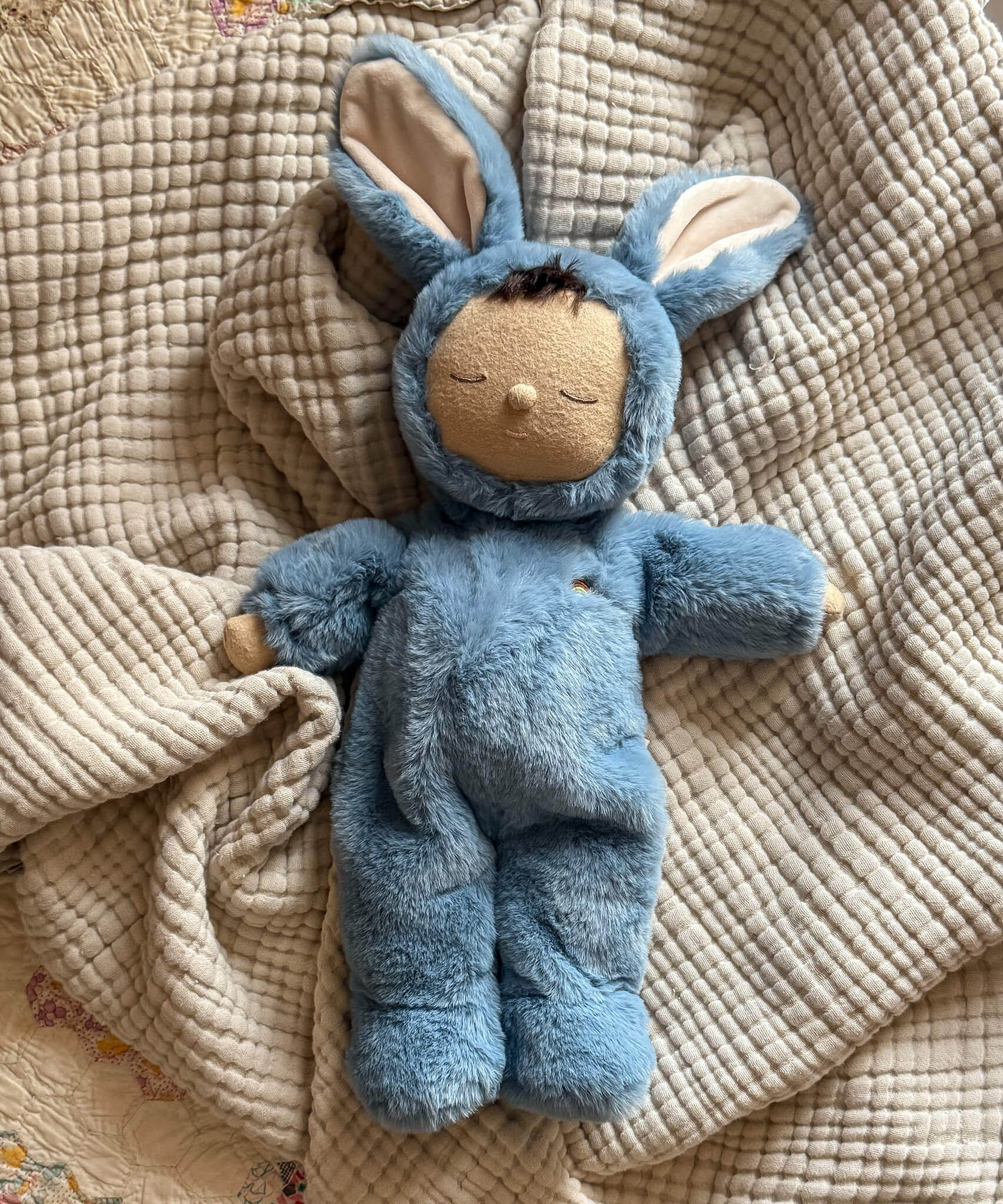 Olli Ella cozy dinkum bunny twiggy doll in blue colour lying on top of a soft blanket. This fluffy toy doll is available at Babipur