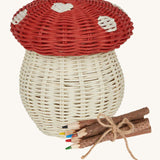 An Olli Ella Porcini mushroom shaped Basket with a red spotted lid, and wooden twig colouring pencils wrapped together with string next to it pictured on a cream background