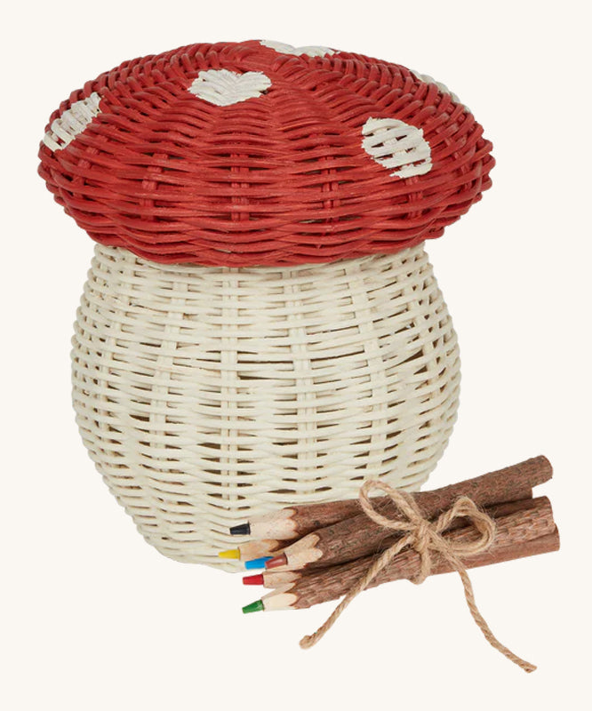 An Olli Ella Porcini mushroom shaped Basket with a red spotted lid, and wooden twig colouring pencils wrapped together with string next to it pictured on a cream background