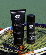 The Green People Sports+ Sun Cream and the Green People Cooling Moisturiser are both stood on top of a tennis racket, with a green playing field in the background