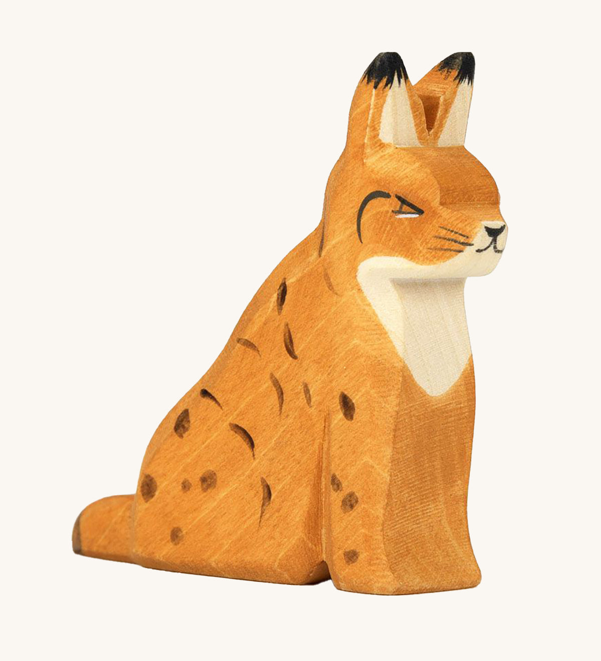 Ostheimer Wooden Sitting Lynx Toy. A beautifully handmade and crafted Wooden Lynx figure with delicate black spots, ear tips and face, with an orange body and natural wood chest. The lynx is sitting on a cream background