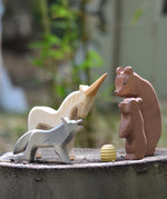 Ostheimer Bear with Cub, Howling Wolf, and Unicorn wooden figures gathered around a beehive, handmade in Germany, natural play scene on tree stump, Waldorf small world toy, sold at Babipur