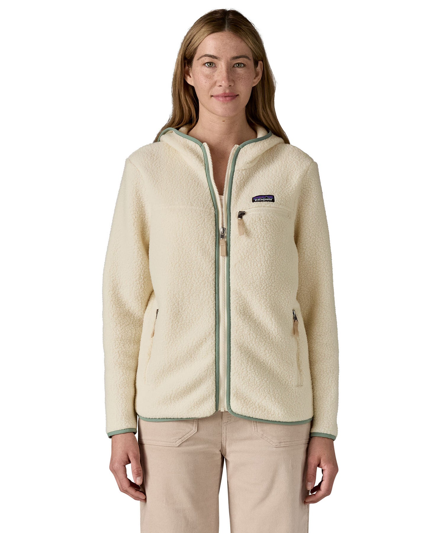 A woman wearing the Patagonia Retro Pile Hoody available at Babipur. A women's fleece style jacket in a light cream colour with green trim. Features a full length zip, 2 side pockets, a chest pocket and a logo patch stitched on the left chest.