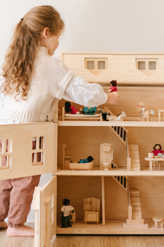 Child playing with a PlanToys Victorian wooden dollhouse filled with miniature furniture and dolls.