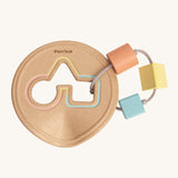 The PlanToys Shape Sorter, is a perfect first shape sorter toy for little ones and babies. Offering a sensory and educational experience, this shape sorter is in a disk shape, was a circle, triangle and square cut out. Attached to the cut out with thing and durable rope is a peach circle block, a yellow triangle block and a blue square block. The image is on a cream background