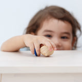 A child holding the PlanToys Mini Spinning Tops in their hand on a wooden table top
