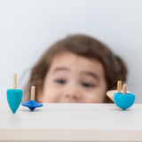 A child looking at the PlanToys Mini Spinning Tops whilst they are spinning on a wooden table top