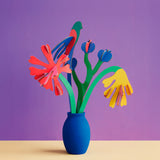 Studio roof small small paper bloom Matisse bouquet with  available at Babipur displayed in a blue vase against a purple background