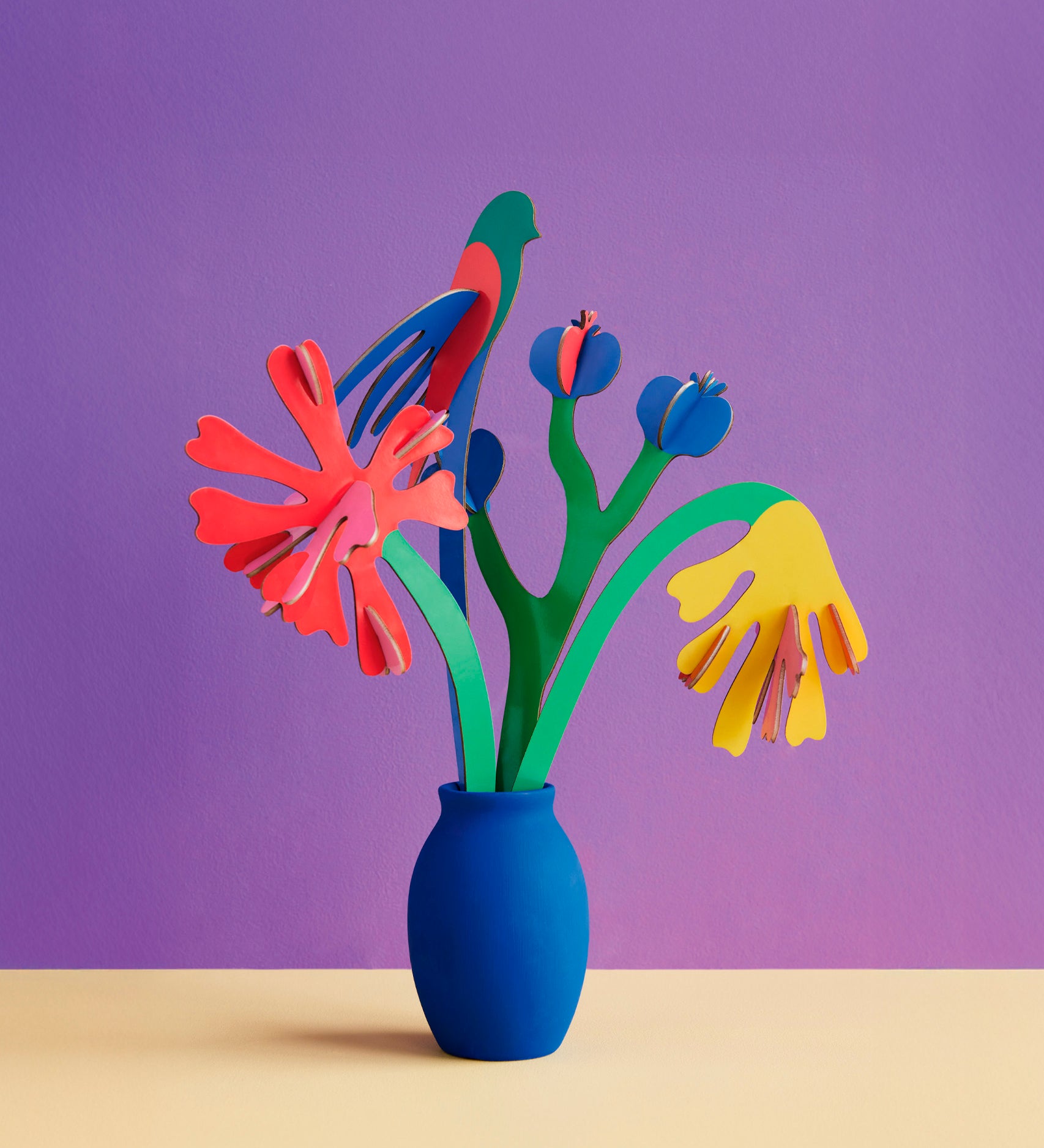 Studio roof small small paper bloom Matisse bouquet with  available at Babipur displayed in a blue vase against a purple background