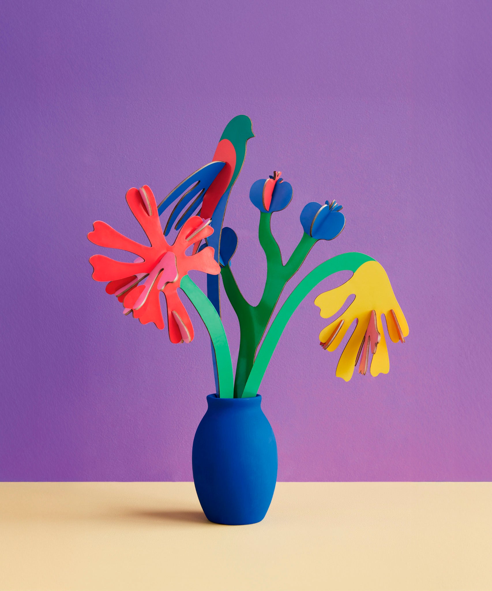Studio roof small small paper bloom Matisse bouquet with  available at Babipur displayed in a blue vase against a purple background