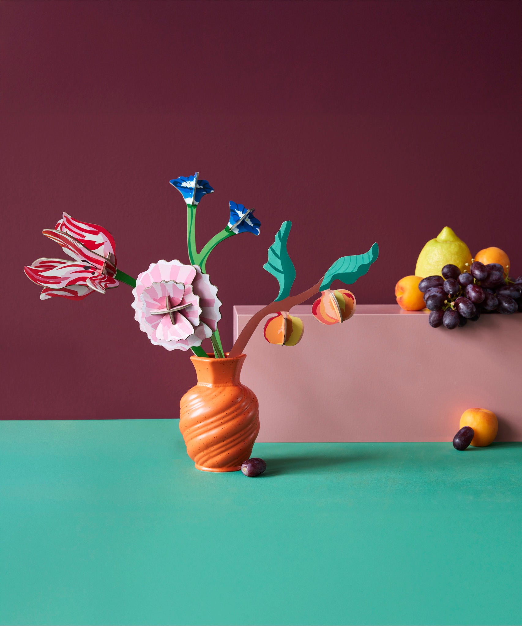 Studio roof small Dutch masters inspired bouquet decoration available at Babipur displayed in a orange vase next to a bunch of fruit