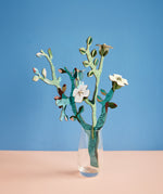 Studio roof small Van Gough inspired bouquet with almond blossom decoration available at Babipur displayed in a glass against a blue background.