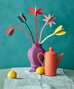 Studio Roof cardboard bouquet in blooming abundance colour way available at Babipur. A DIY kit made from cardboard displayed in a homemade paper mache vase next to a watering can