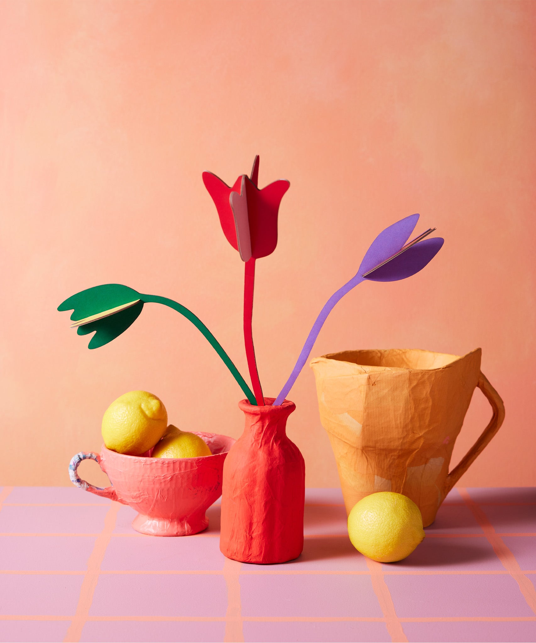 Studio Roof cardboard bouquet in tulip love colour way available at Babipur. A DIY kit made from cardboard displayed in a homemade red paper mache vase next to a watering jug and fruit bowl