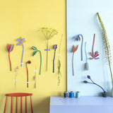 A lovely display using the different coloured flowers from the Studio Roof cardboard bouquet giant set available at Babipur. These flowers are taped up on a wall above a red chair and blue table
