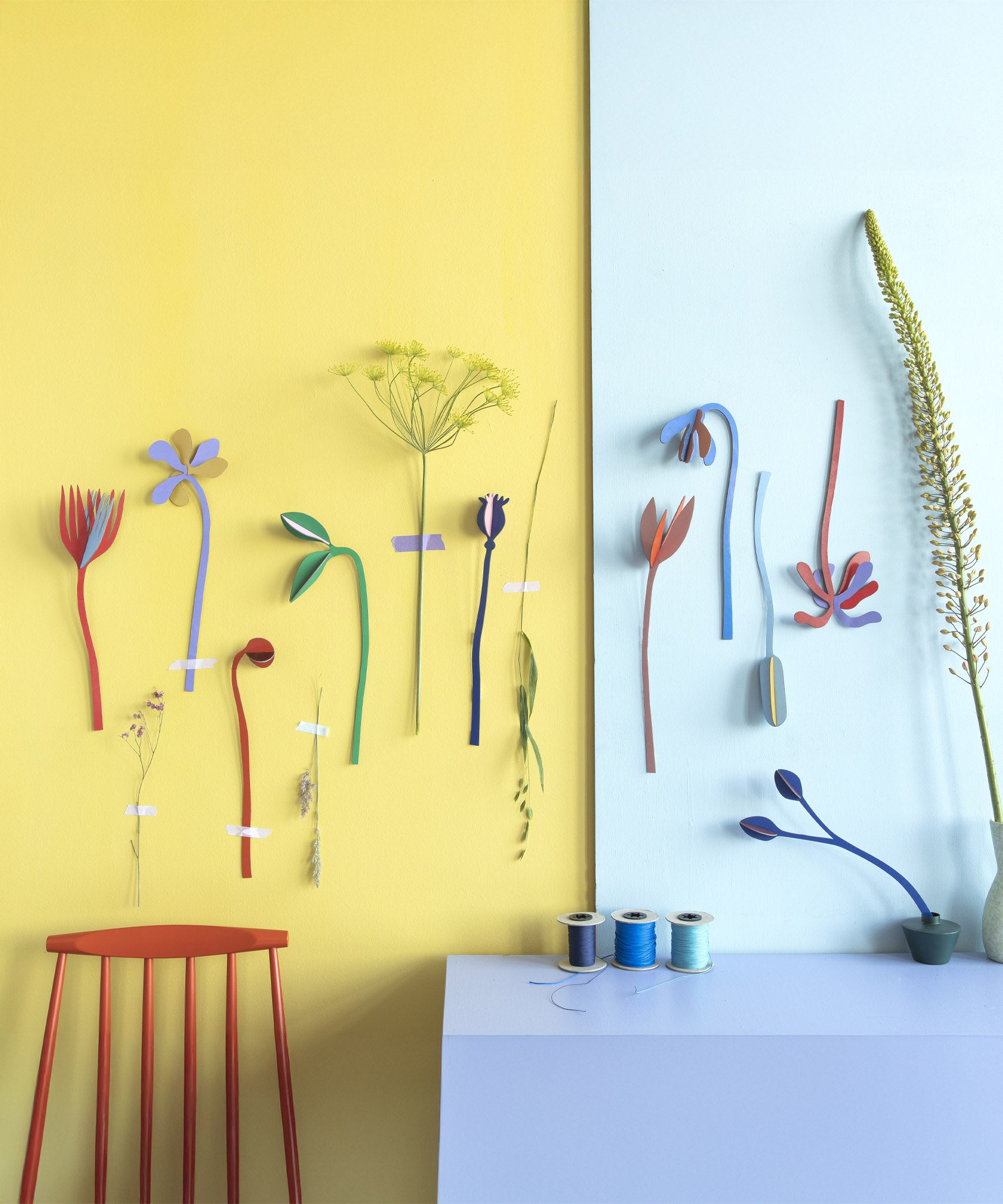 A lovely display using the different coloured flowers from the Studio Roof cardboard bouquet giant set available at Babipur. These flowers are taped up on a wall above a red chair and blue table