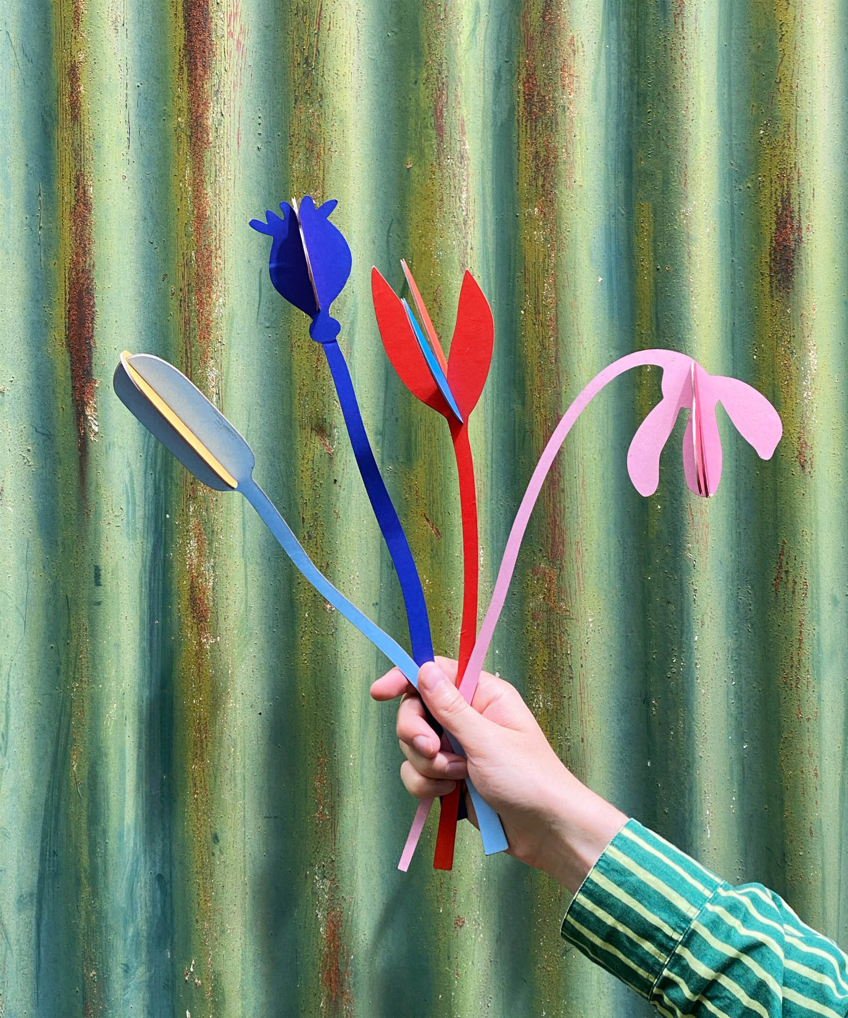A hand holding a bunch of the Studio Roof cardboard bouquet from the giant set showing scale. This set is available at Babipur.