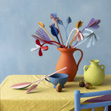 Studio Roof giant cardboard bouquet in available at Babipur. A DIY kit made from cardboard in a shape of different coloured flowers. This set is displayed on a table in a home made red vase.