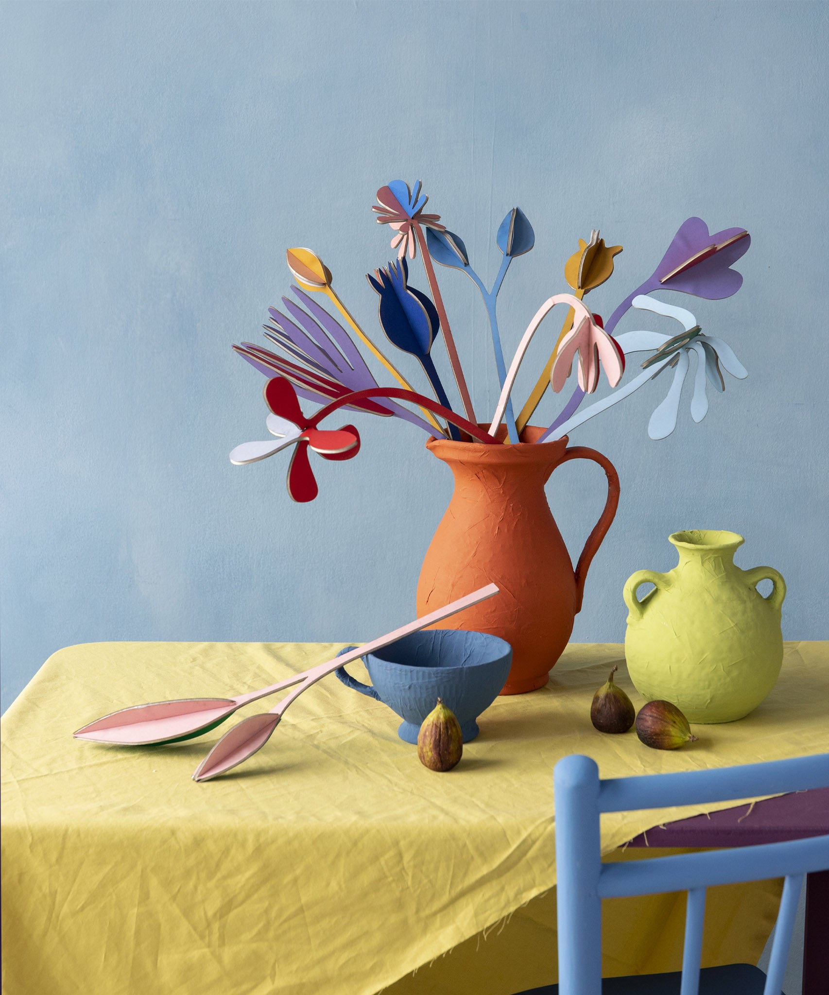 Studio Roof giant cardboard bouquet in available at Babipur. A DIY kit made from cardboard in a shape of different coloured flowers. This set is displayed on a table in a home made red vase.