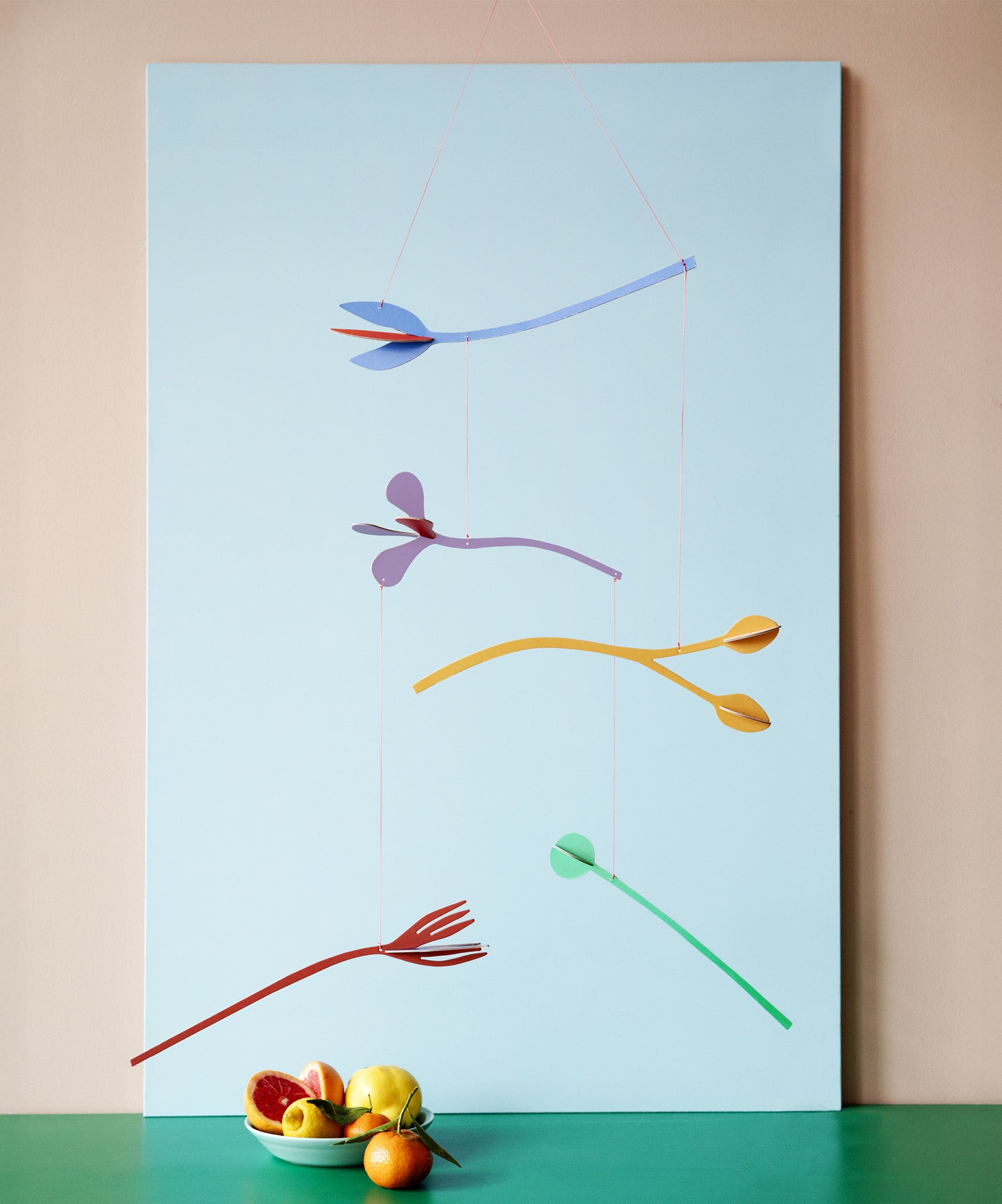 A Studio Roof cardboard Cordelia floral art mobile hanging over a table. This multicoloured floral DIY cardboard set is available at Babipur.