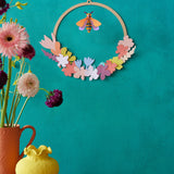 A decorative display with Studio Roof wreath meadow with bee available at Babipur. A DIY kit made from cardboard thats hanging on a wall