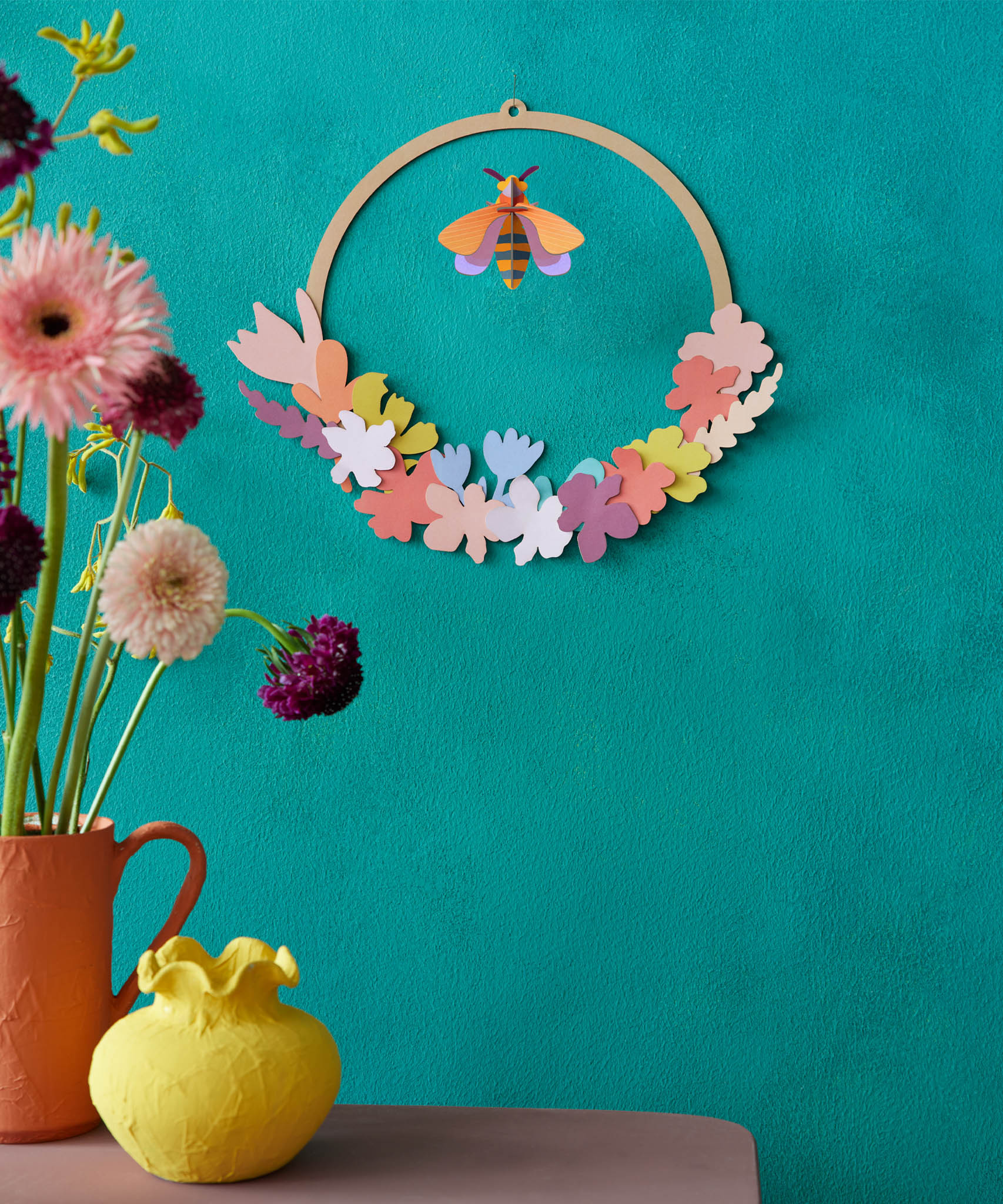 A decorative display with Studio Roof wreath meadow with bee available at Babipur. A DIY kit made from cardboard thats hanging on a wall
