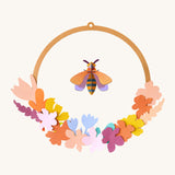 Studio Roof wreath meadow with bee available at Babipur. A DIY kit made from cardboard in a floral wreath design with a bee hanging from the loop.