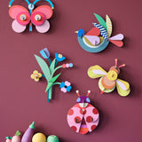 A group of wall decorations from the collaboration with Studio Roof and Zoe Miller available at Babipur. Decorations are hanging on a wall above wooden vegetables