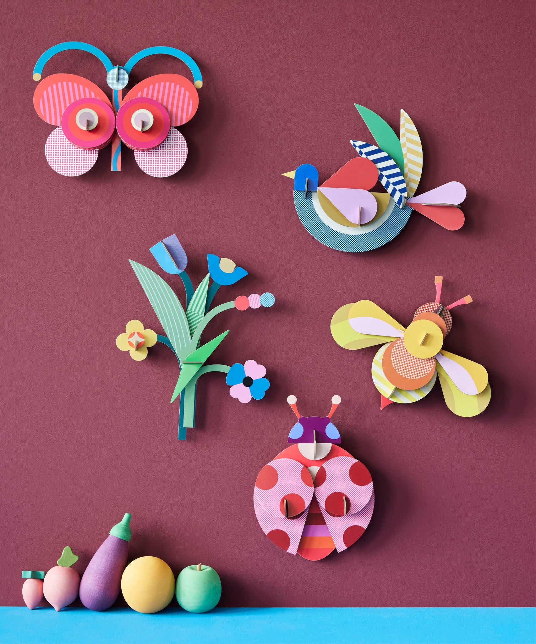 A group of wall decorations from the collaboration with Studio Roof and Zoe Miller available at Babipur. Decorations are hanging on a wall above wooden vegetables