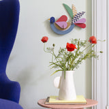 Feathery bird wall decoration available at Babipur hanging on a wall above a white vase with flowers. A Studio roof collaboration with artist Zoe Miller.
