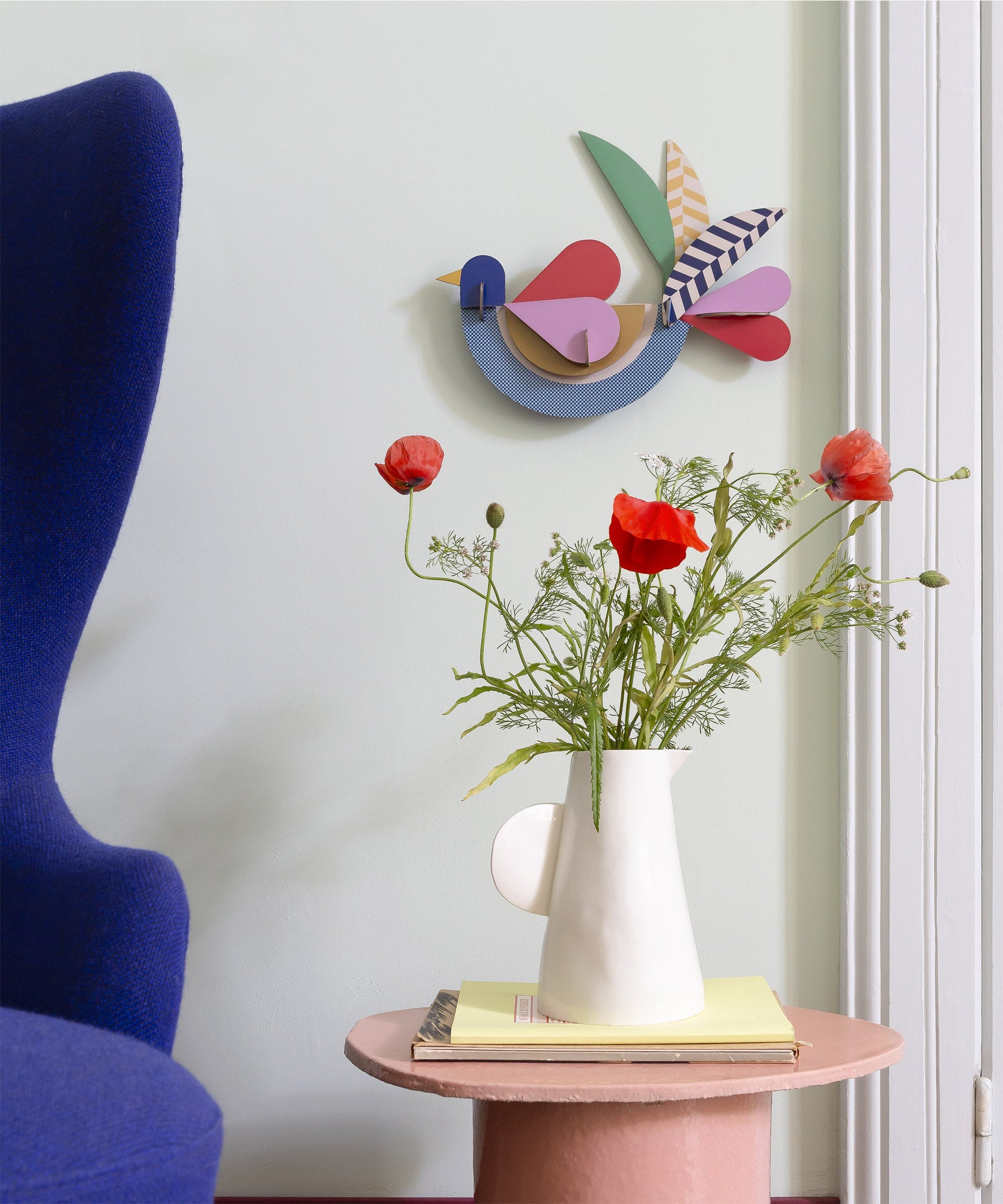 Feathery bird wall decoration available at Babipur hanging on a wall above a white vase with flowers. A Studio roof collaboration with artist Zoe Miller.