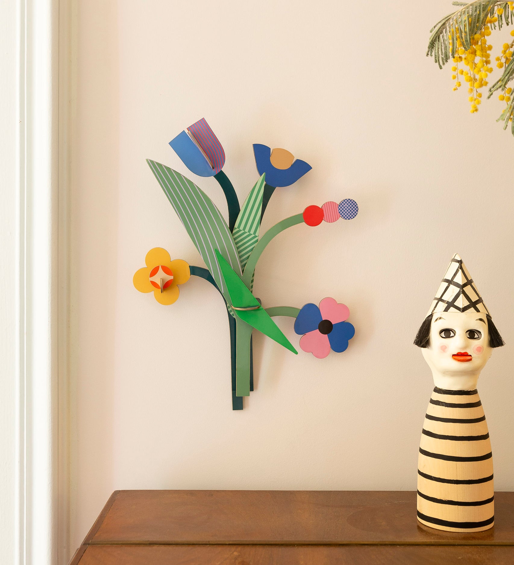 Daisy belle wall decoration available at Babipur hanging on a wall above above a wooden drawer next to a giant wooden peg doll. A Studio roof collaboration with artist Zoe Miller.