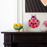 Dotted lady wall decoration available at Babipur hanging on a wall above a mantlepiece next to a bowl of lemons and pots. A Studio roof collaboration with artist Zoe Miller.