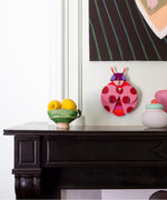 Dotted lady wall decoration available at Babipur hanging on a wall above a mantlepiece next to a bowl of lemons and pots. A Studio roof collaboration with artist Zoe Miller.