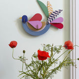 A close up of the feathery bird wall decoration available at Babipur hanging on a wall above red poppies
