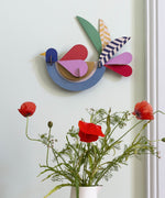 A close up of the feathery bird wall decoration available at Babipur hanging on a wall above red poppies