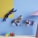 3 Studio Roof 3D Cardboard Models of Wildlife Animals on a blue and yellow all - the Panther, Zebra and the Rhino. Surrounded by decorative objects on a table, replicating a home setting.
