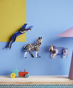 3 Studio Roof 3D Cardboard Models of Wildlife Animals on a blue and yellow all - the Panther, Zebra and the Rhino. Surrounded by decorative objects on a table, replicating a home setting.