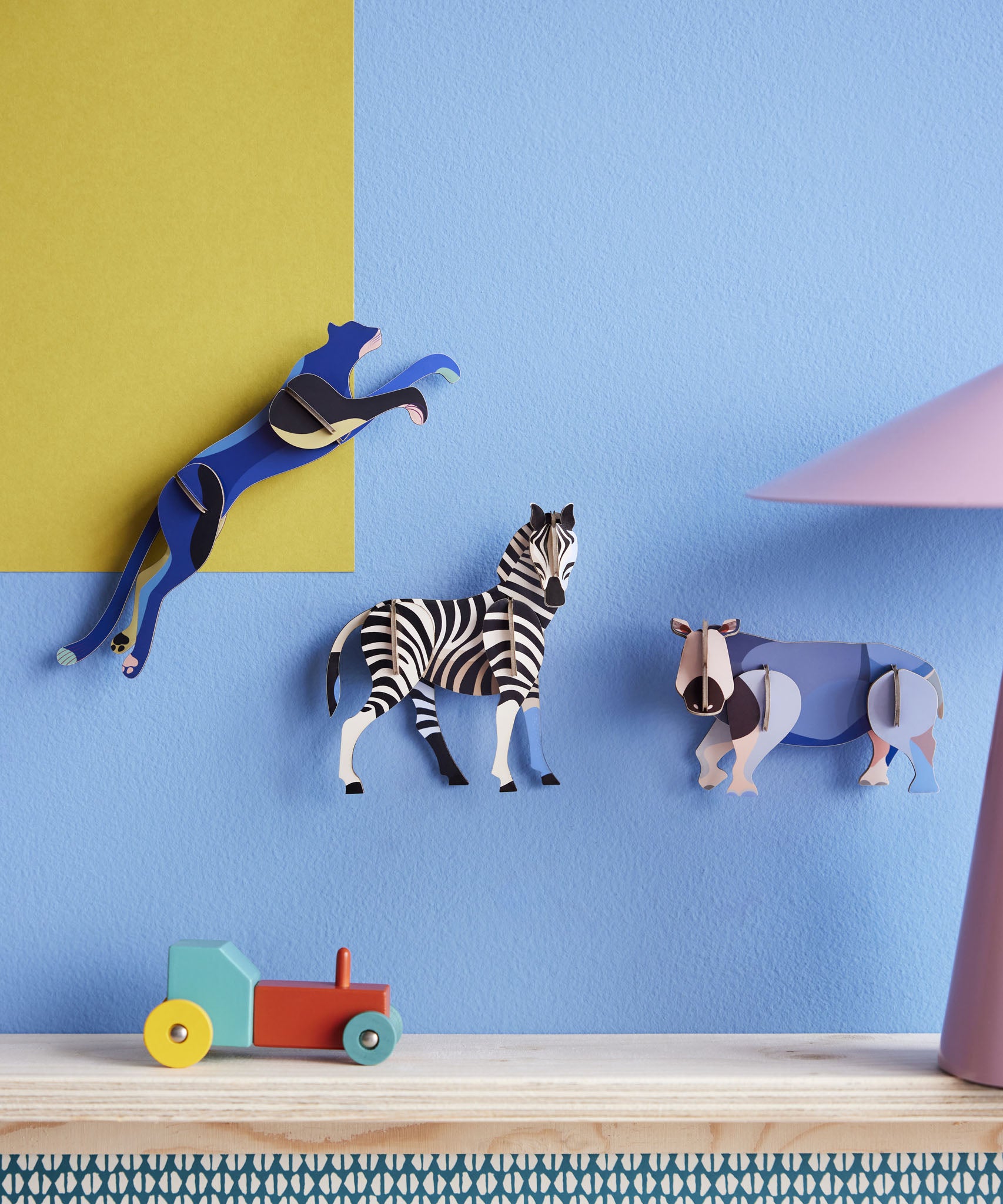 3 Studio Roof 3D Cardboard Models of Wildlife Animals on a blue and yellow all - the Panther, Zebra and the Rhino. Surrounded by decorative objects on a table, replicating a home setting.