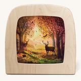 A Toverlux silhouette inside a wooden  lamp. This silhouette has 2 stag deers in an Autumn woodland scene. This layered paper style silhouette is by artist Vogel Geluk and available at Babipur.