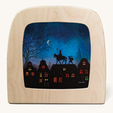 A Toverlux silhouette inside a wooden  lamp. This silhouette has St Nicholas on a horse on top of a roof undr a moonlit sky with an elf following. This layered paper style silhouette is by artist Vogel Geluk and available at Babipur